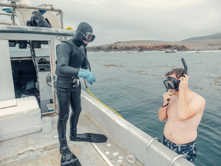 Two divers get ready for an underwater expedition. A man in a wetsuit is on a boat, while another prepares with a snorkel.